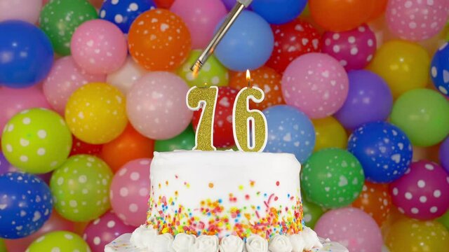 Cake with burning candles number 76. A tasty celebration cake on a bright festive background of colorful balloons.