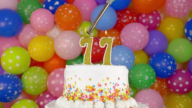 Cake with burning candles number 77. A tasty celebration cake on a bright festive background of colorful balloons.