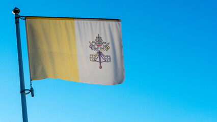 Weaving flag of the country Vatican City on a flagpole in front of blue sky with lens flare. Christianity concepts.