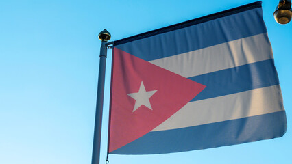 National flag of Cuba on a flagpole in front of blue sky with sun rays and lens flare. Diplomacy concept.