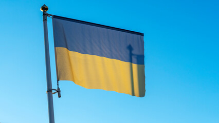 National flag of Ukraine on a flagpole in front of blue sky with sun rays and shadow of flagstaff. Diplomacy concept.
