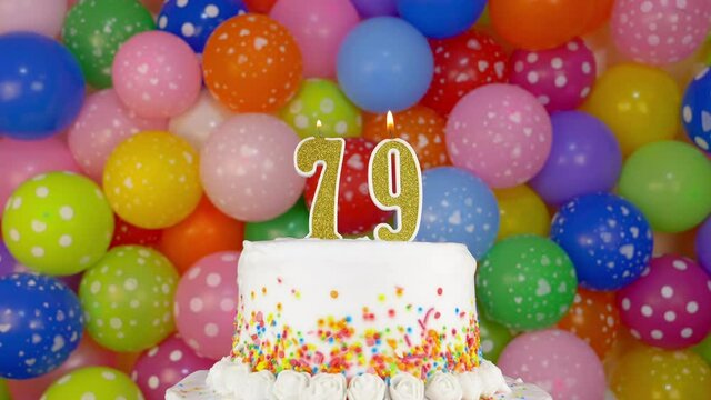 Cake with burning candles number 79. A tasty celebration cake on a bright festive background of colorful balloons.