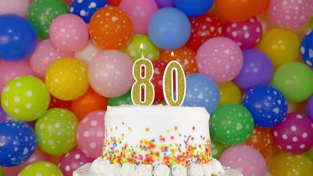 Candles in the form of number 80 on the Birthday cake. A tasty celebration cake on a bright festive background of colorful balloons.