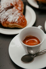 The table with sweets (pastries: croissant, cookies), white cups (mug) with hot black coffee (espresso), the saucer, the spoons at a local bar. Traditional Italian breakfast. Milan, Lombardy, Italy