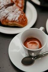The table with sweets (pastries: croissant, cookies), white cups (mug) with hot black coffee (espresso), the saucer, the spoons at a local bar. Traditional Italian breakfast. Milan, Lombardy, Italy