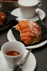 Traditional Italian breakfast. Fresh croissants with cream and sugar powder, espresso coffee and cappuccino on a black wooden table in Milan, Lombardy, Italy. European food and pastry.