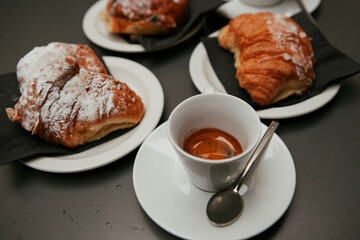 The table with sweets (pastries: croissant, cookies), white cups (mug) with hot black coffee (espresso), the saucer, the spoons at a local bar. Traditional Italian breakfast. Milan, Lombardy, Italy