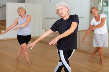 Obraz premium Positive aged woman practicing vigorous dance movements in group dance class .