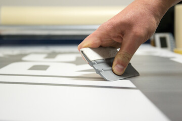 Close-up of a man's hand holding a trowel and preparing to make car stickers on vinyl - obrazy, fototapety, plakaty