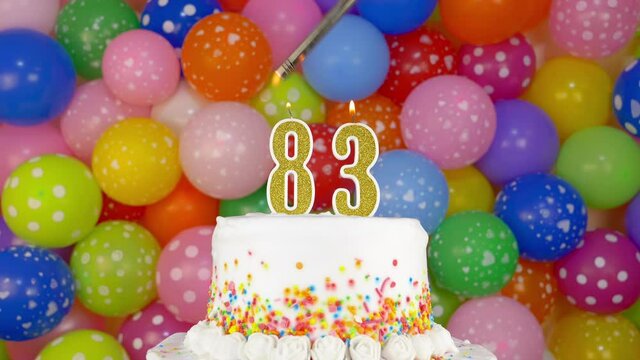 Cake with burning candles number 83. A tasty celebration cake on a bright festive background of colorful balloons.