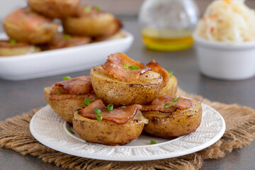Golden potato halves baked with onion and bacon served on a white plate. Dark background, selective focus, close up.