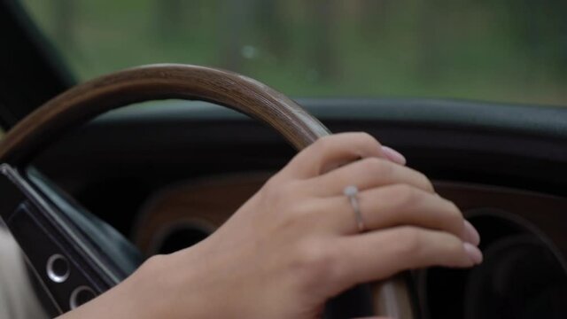 Young woman is touching the wooden steering wheel in the car. Old retro car. The girl driver is married. Wife with a wedding ring on her finger.