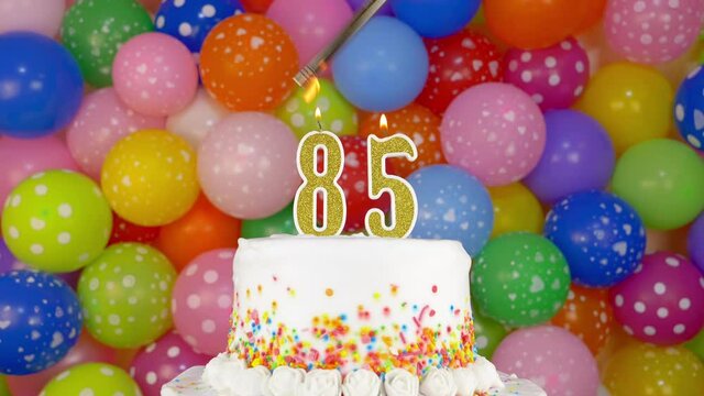 Cake with burning candles number 85. A tasty celebration cake on a bright festive background of colorful balloons.