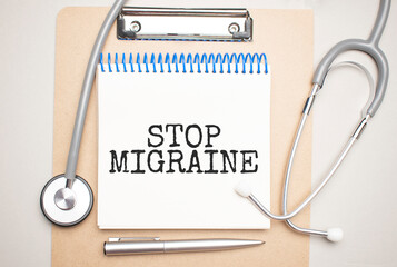 White notepad with the words STOP MIGRAINE and a stethoscope on a blue background. Medical concept