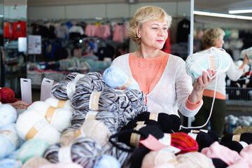 Fototapeta na wymiar Happy cheerful positive smiling mature woman buyer choosing colored yarn for knitting on sale