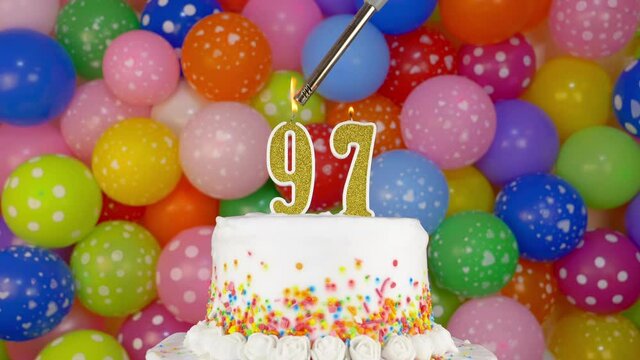 Cake with burning candle number 97. A tasty Birthday Cake on a bright festive background of colorful balloons.