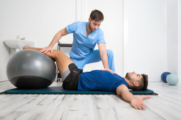 Fototapeta na wymiar Physiotherapist helps handsome young patient with pilates exercises. High quality photo