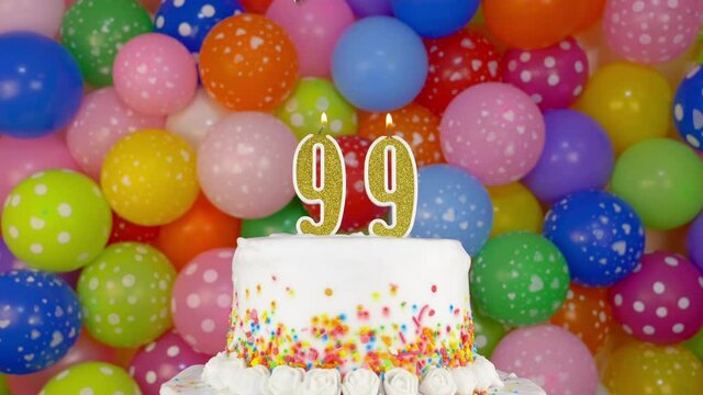Cake with burning candle number 99. A tasty Birthday Cake on a bright festive background of colorful balloons.