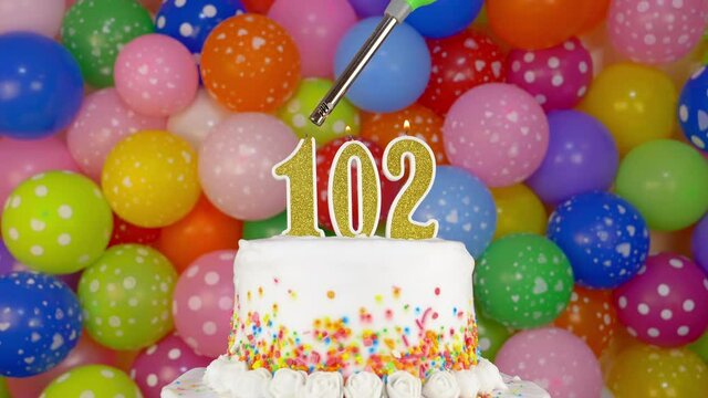 Cake with burning candles number 102. A tasty Birthday Cake on a bright festive background of colorful balloons.