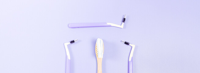 Bamboo toothbrush with toothpaste and three small toothbrushes on a soft lilac background