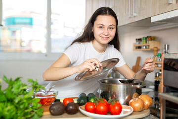 Young woman preparing soup in saucepan in the kitchen