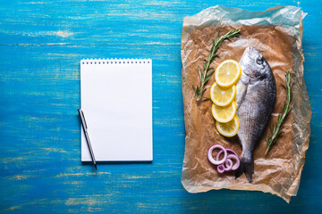 Fresh raw Dorado fish on cooking paper with spices and a notebook for recipe or menu.