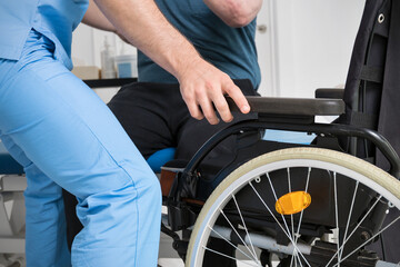 Male Physiotherapist helping a patient with a disability who uses a wheelchair to get up at rehabilitation hospital. High quality photo.