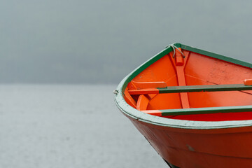 A bright, colorful, orange and green wooden fishing vessel, wood boat, on the bay. There's fog,...