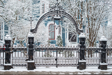 A vintage decorative black wrought iron fence with a large arched gate in the foreground. There's a...