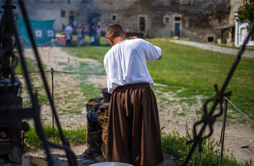 Medieval man in baggy clothes cooks food in a cauldron