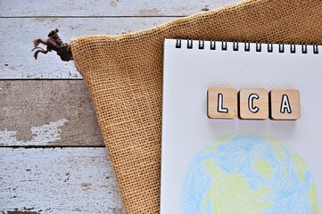 The letters arranged in the word LCA It's an abbreviation for Life Cycle Assessment. It's on a wihte wooden board with an illustration of the earth.