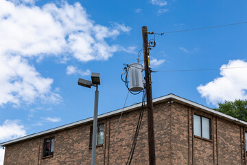 Obraz premium View looking up at the corner and roofline of a generic apartment building, exterior lighting and power pole with transformer, horizontal aspect