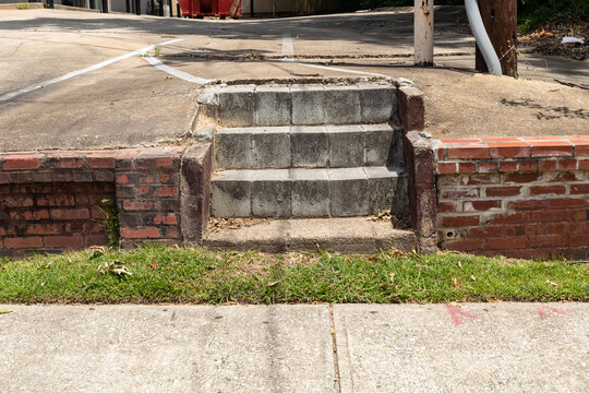 Straight on view of narrow concrete block stairs between a sidewalk and a paved parking lot, horizontal aspect
