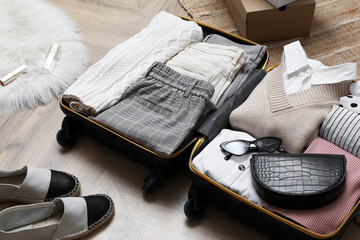 Open suitcase with folded clothes, accessories and shoes on floor