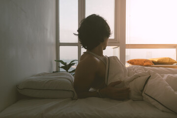 Asian man just wake up in a happy morning in bright white bedroom.