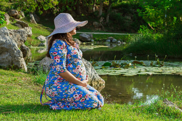 Mujer embarazada en orilla de lago mientras toca su vientre al aire libre, concepto de maternidad