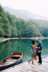 Pregnant woman and man stand on the pier by the lake near a moored boat