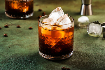 Black russian cocktail, trendy alcoholic drink with vodka, coffee liqueur and ice, rusty green dark background, bar tools