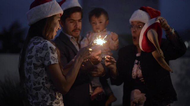 Latin family celebrating christmas new year holidays having fun with sparklers at dawn wearing Santa Claus hats
