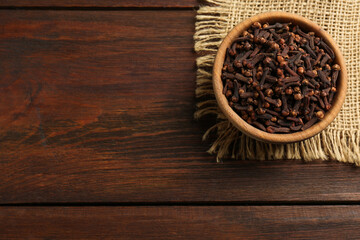 Aromatic dry cloves in bowl on wooden table, top view. Space for text