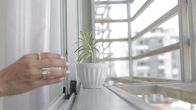 Toma cerrada. Chica joven retira su planta en la ventana para toma de sol. Camara lenta