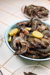 Raw Whole Fresh Uncooked Prawns Shrimps on Enamel plate, White Ceramic Background. Front View with Lemon Slice