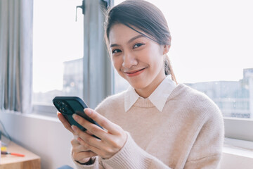Fototapeta na wymiar Young Asian woman using smartphone at home