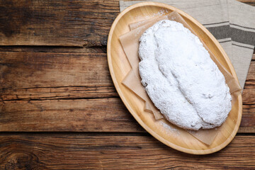 Plate of delicious Stollen sprinkled with powdered sugar on wooden table, top view. Space for text