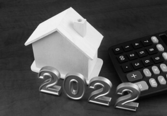 Wooden house and calculator with numbers 2022 on table. Real estate price in 2022 concept.