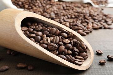 Scoop with roasted coffee beans on wooden table, closeup