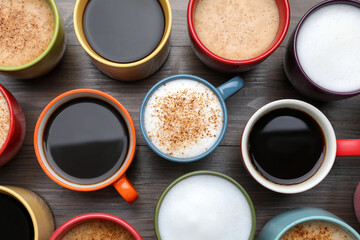 Many different cups with aromatic hot coffee on wooden table, flat lay