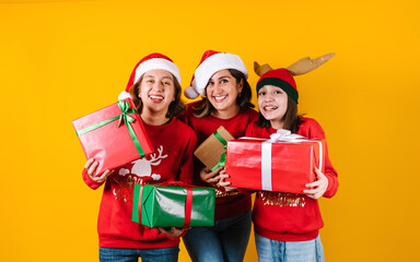 Portrait of Latin mother and daughters holding Christmas gift box on a yellow background in Mexico latin america