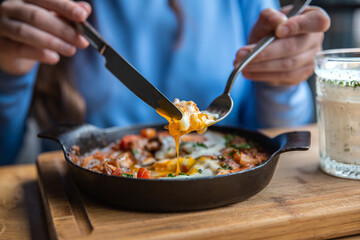 Close-up, a woman in a cafe dines on traditional shakshuka.