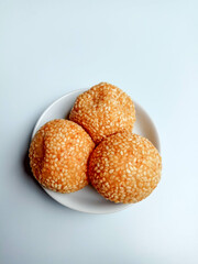 Three fried sesame balls with mung beans filling, called onde-onde in Indonesia, placed in a white small plate.